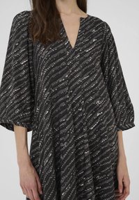 Schwarzes Kleid mit V-Ausschnitt und Ballonärmeln, das ein strukturiertes Wellenmuster in Grau und Weiß aufweist. Weicher Stoff. Mid-Length-Design.