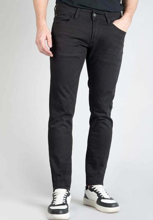 Black slim-fit jeans made of denim, featuring a classic five-pocket design, and paired with white and black lace-up sneakers.