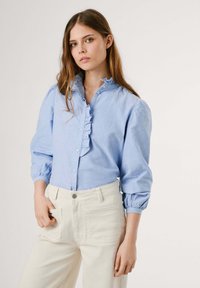 Lichtblauwe, knoopsluiting shirt met gerimpelde kraag en knopenlijst, lange pofmouwen, gemaakt van katoen. Gecombineerd met crèmekleurige wijd uitlopende broek.