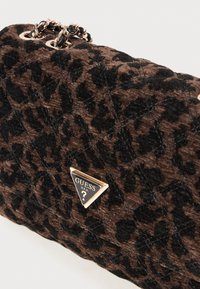 Bolso acolchado con estampado de leopardo marrón y negro, con cadenas doradas y una placa triangular del logo de Guess en la parte frontal.