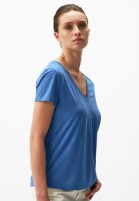 Niebieska koszulka z dekoltem w kształcie litery V, z krótkimi rękawami, wykonana z gładkiego, lekkiego materiału. Prosty design, bez wzorów i haftów.