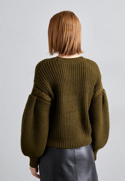Dunkelgrüner gestrickter Pullover mit ribbeliger Textur und Ballonärmeln. Verfügt über einen runden Ausschnitt und einen kurzen Saum, kombiniert mit einem glatten schwarzen Rock.
