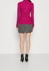 Pull à col montant fuchsia avec des accents à rayures horizontales, associé à une mini jupe en vichy noir et blanc et des bottines noires.