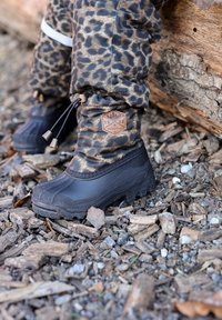 Bottes imperméables noires avec une tige à imprimé léopard, dotées d'un haut resserré, d'une étiquette en cuir de marque et de semelles en caoutchouc texturé sur une surface naturelle.