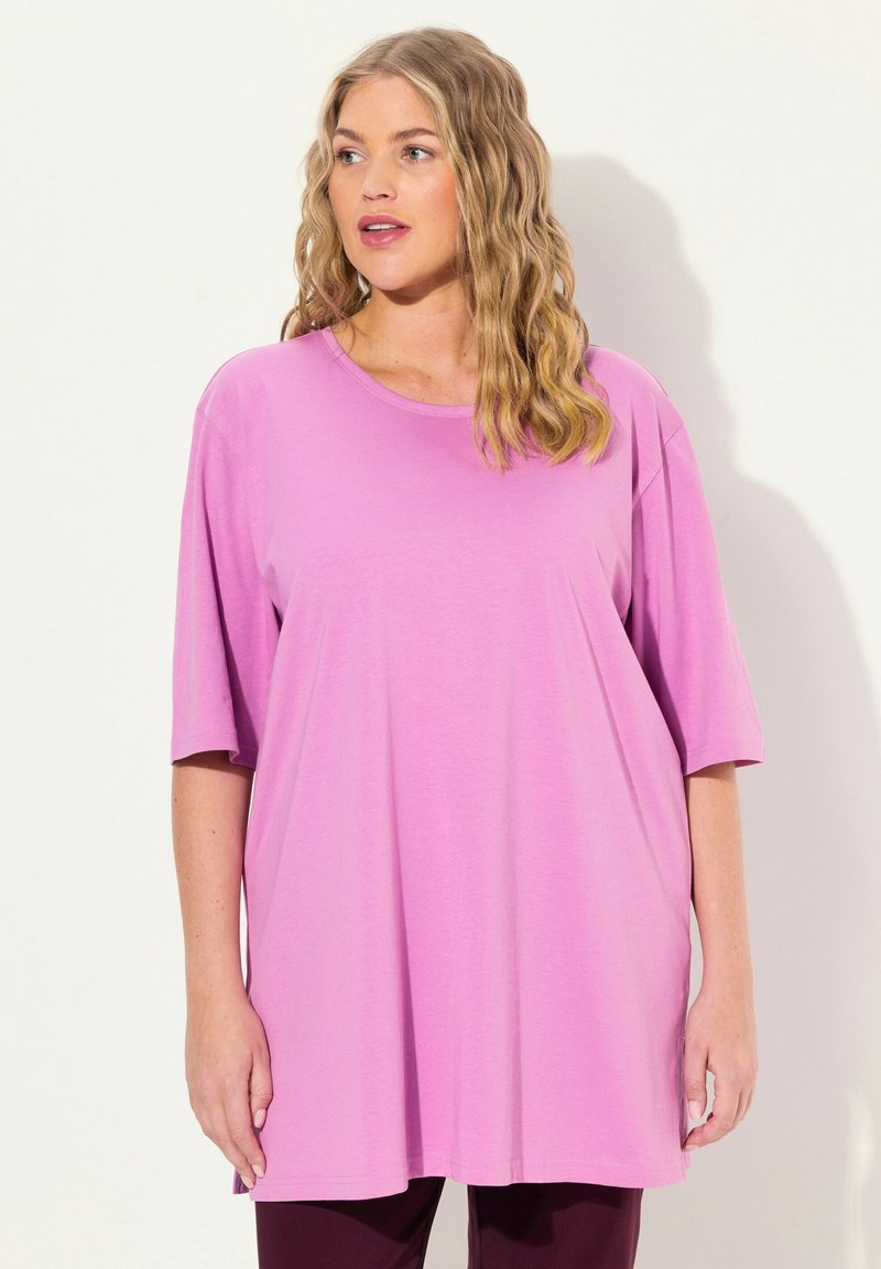 Leichtes, kurzärmliges Oberteil aus einfarbigem rosa Stoff. Mit rundem Ausschnitt und oversized Schnitt. Weiche Textur mit lockerer Passform.