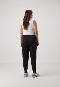 Joggers noirs avec une taille ajustée, des poignets resserrés et une texture lisse. Un débardeur blanc complète la tenue. Style athlétique décontracté.