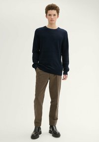 Granatowy sweter o fakturze z długim rękawem, zestawiony z brązowymi spodniami w kratę i czarnymi, masywnymi botkami za kostkę. Prosty i nowoczesny design.