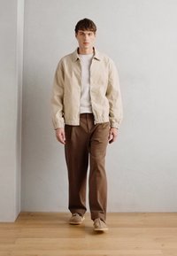 Beige bombázó dzseki, fehér crewneck póló, barna nadrág és bézs cipő. Sima anyag, laza szabás és rugalmas mandzsetták. Minimalista dizájn.