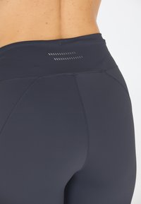Leggings a vita alta di colore blu navy realizzati in tessuto elasticizzato, con una texture liscia e dettagli delle cuciture sottili. Accenti riflettenti in vita.