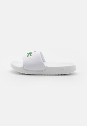 Sandale blanche à glissière en matériau synthétique, arborant un logo crocodile vert sur la bride et une semelle texturée pour une meilleure adhérence.