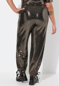 Zwarte en gouden pailletten joggers met een fitted ontwerp, elastische boorden en een geplooide tailleband, gecombineerd met glanzende zwarte veterschoenen tot de enkel.