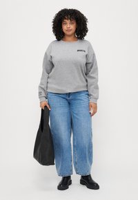 Gray sweatshirt with "BROOKLYN" text, paired with blue wide-leg jeans. Black ankle boots and a black tote bag complete the look.