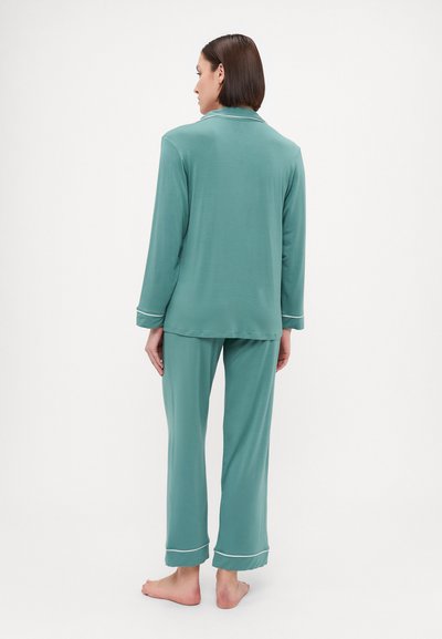 Turquoise pajama set with long sleeves and pants. Features white piping along the collar and cuffs. Soft, lightweight fabric.
