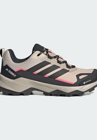 Μπεζ και μαύρο πεζοπορικό παπούτσι Adidas Terrex με ροζ λεπτομέρειες, μαύρα κορδόνια, ανθεκτική σόλα και αδιάβροχο υλικό Gore-Tex.