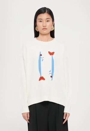 Vit stickad tröja med broderade blå och röda fiskmotiv på framsidan, med avslappnad passform och ribbade manschetter och nederkant.