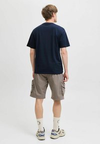 Jūros pajėgų medvilninis t-shirt, trumpomis rankovėmis, derinamas su šviesiai smėlinėmis krovinių šortais, turinčiais šonines kišenes. Dėvimi su baltais kojiniais ir šviesiais sportiniais bateliais.