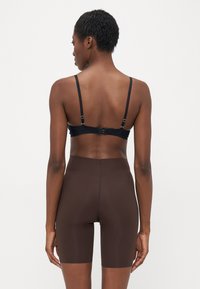 Zwarte bralette met dunne bandjes en verstelbare hardware, gecombineerd met donkerbruine high-waisted shorts, gladde textuur, figuurvormend ontwerp.