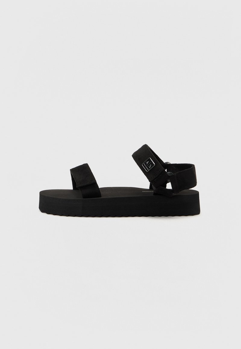 Sandales noires avec deux sangles en tissu et une semelle texturée. Elles présentent une plateforme épaisse et plate ainsi qu'un petit logo de la marque sur la sangle latérale.