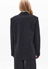 Blazer de rayas finas en color oscuro con un ajuste entallado, que presenta un cuello con muescas y una abertura trasera sencilla. Confeccionado en un tejido texturizado con un acabado suave.