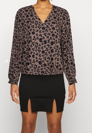 Braune Bluse mit floralen Mustern in Schwarz und Blau, V-Ausschnitt und langen Ärmeln, kombiniert mit einem schwarzen Minirock mit seitlichen Schlitzen.