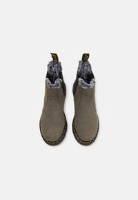 Grå suede Chelsea-støvler med en fluffy sort og grå fôr, elastiske sidepaneler og gul søm langs den svarte sålen.