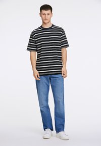 Camiseta de manga corta a rayas en navy y blanco, combinada con jeans azules y zapatillas blancas, con cuello redondo y corte relajado.