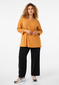 Sennepsgul ribbet langærmet bluse med en afslappet pasform, parret med sorte brede bukser og beige sneakers.