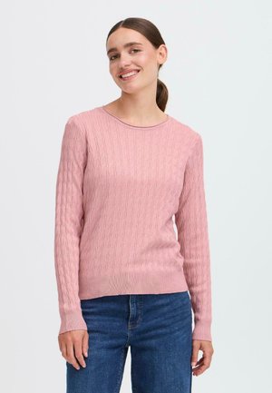 Un pull rose clair avec un motif en tricot à câbles texturé, un col rond, des poignets et un ourlet côtelés, associé à un jean en denim bleu.