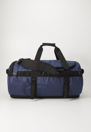 Sac de sport navy en tissu durable, avec des sangles noires, une bandoulière amovible et une pochette zippée sur le côté.
