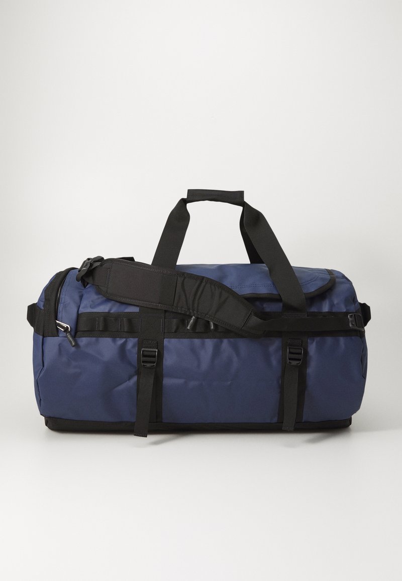 Navy duffle bag made of durable fabric, featuring black straps, a detachable shoulder strap, and a zippered pocket on the side.