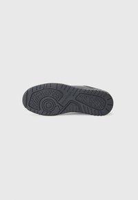 Semelle de chaussure en caoutchouc noir avec des motifs de grip texturés et un dessin circulaire près de la plante du pied, marquée du texte « "HILFIGER" ».