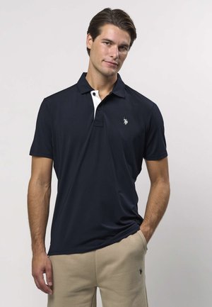 Lahtise lõikega tumesinine polo-särk hingavast kangast, millel on valge kontrastvärvi krae, lühikesed varrukad ja vasakul rinnal väike logo.