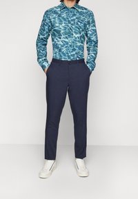 Camicia a maniche lunghe con un motivo ad acqua blu, abbinata a pantaloni navy e sneaker bianche. Vestibilità classica con colletto button-down.