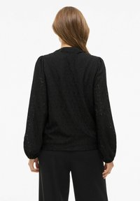 Czarna bluzka z teksturowanym wzorem o otwartym splocie, długimi bufkami oraz luźnym krojem, z zaokrąglonym dekoltem i subtelnymi zdobieniami.