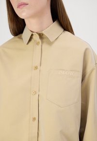 Khaki oversized button-up shirt, cotton material, point collar, chest pocket with "2NDDAY" embroidery, featuring light brown buttons.