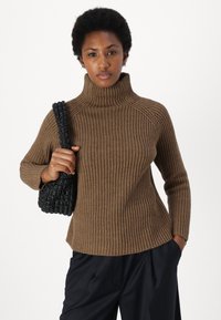 Brauner gerippter Rollkragenpullover mit lockerer Passform und langen Ärmeln, kombiniert mit einer schwarzen geflochtenen Handtasche. Die Textur scheint weich und gemütlich zu sein.