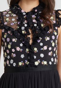 Vestido negro con un corsé transparente y bordado que presenta patrones florales en tonos pastel, bordes de encaje con volantes y una cintura ajustada.