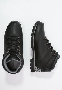 Stivali da hiking neri con parte superiore in pelle, fodera grigia e suola robusta. Presentano occhielli metallici e un logo sul tallone.