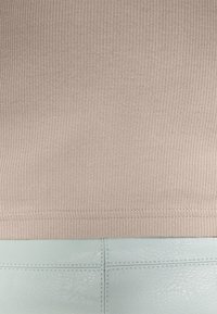 Top de tecido canelado bege combinado com uma parte inferior de couro liso azul-claro, apresentando costuras limpas e um acabamento texturizado.