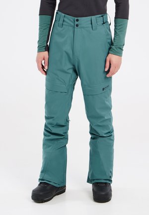 Teal waterdichte sneeuwbroeken met een relaxed fit, ritszakken en versterkte manchetten, gecombineerd met zwarte sneeuwboots.