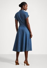 Denim skjortekjole med korte oppbrettede ermer, en innsnevret midje og en svømmende midi-skjørt. Myk blå stoff med subtile sømdetaljer.