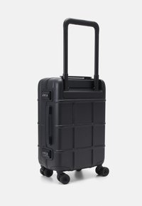 Crna tvrda putna torba s teksturiranom površinom, mrežastim uzorkom, teleskopskom ručkom i četiri rotirajuće kotača za lako kretanje.