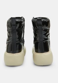 Botas de tobillo negras y brillantes con un diseño voluminoso, que cuentan con una suela gruesa de color beige y una lengüeta trasera para ponerlas fácilmente.