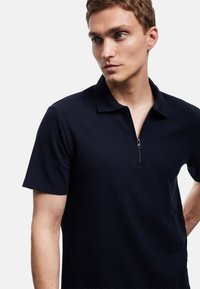 Granatowa koszulka polo z krótkim rękawem o teksturowanym wzorze, z kołnierzem na pół zamek i minimalistycznym designie. Miękka tkanina z luźnym krojem.