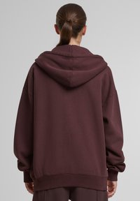 Burgundská oversize mikina vyrobená z bavlneného zmesi, s kapucňou na šnúrku, rebrovanými manžetami a hladkou textúrou. Bez viditeľných log a vzorov.