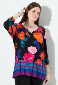 Mustakukkainen toppi kirkkailla vaaleanpunaisilla, oransseilla ja sinisillä kukilla; V-pääntie; 3/4-hihat; kuvioitu helma, jossa on raitoja ja pisteitä.