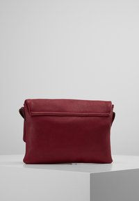 Kabelka z karmínové kůže s texturovaným povrchem, obdélníkového tvaru a se sklápěcí klopou. Obsahuje krátký popruh pro nošení.