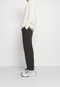 Sweat-shirt beige clair superposé à une chemise vert menthe, associé à un pantalon foncé et des baskets blanches avec des accents gris et des semelles noires.