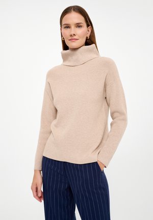 Beige ribbed sweater with a high turtleneck and long sleeves, paired with navy striped trousers. Soft texture, relaxed fit, seamless design.