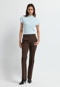 Top en tricot bleu clair à manches courtes avec un motif texturé, associé à un pantalon marron sur mesure et des bottines à talons aiguilles noires.